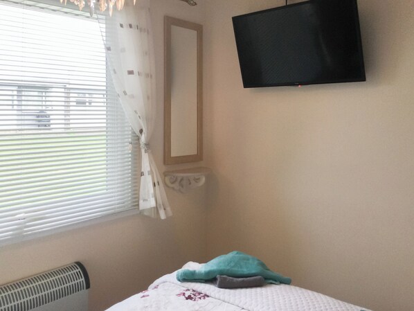 Una habitación con cama, televisor montado en la pared y ventana con persianas.
