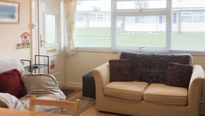 Een woonkamer met een beige bank, een houten tafel en een raam met zonwering.