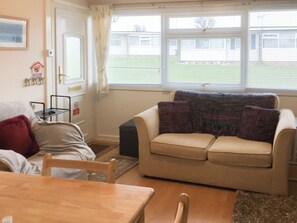 Ein Wohnzimmer mit einem beigen Sofa, einem Holztisch und einem Fenster mit Jalousien.