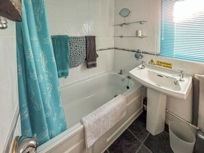 A bathroom with a bathtub, a sink, and a shower. There is a caution sign for hot water.