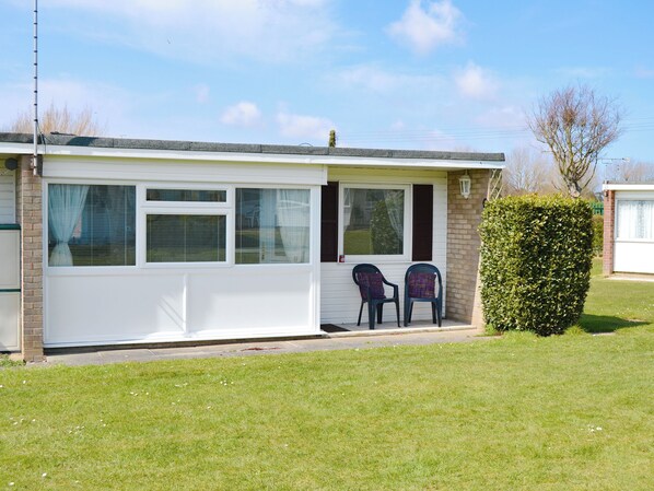 A single-story mobile home with a covered porch, two chairs, and a well-maintained lawn.