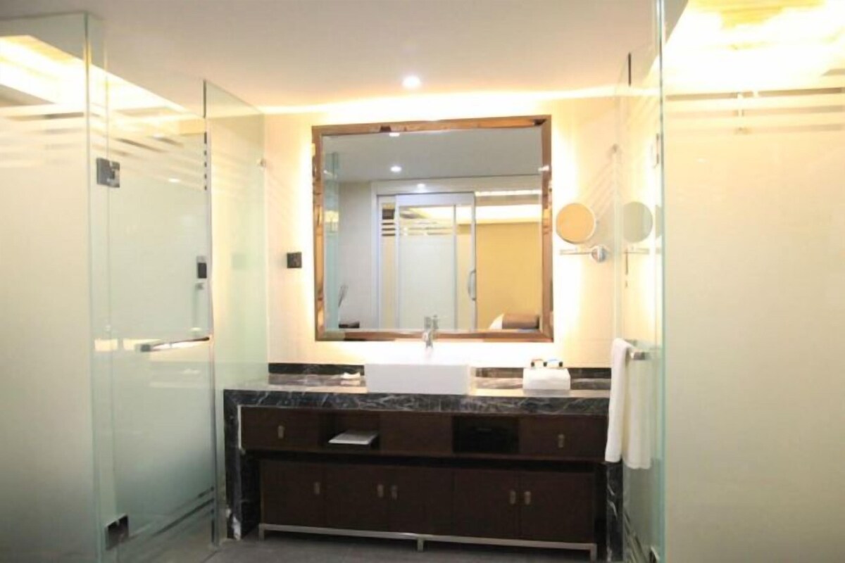 A modern bathroom with a glass shower enclosure, a large mirror, a marble countertop, and dark wooden cabinets.