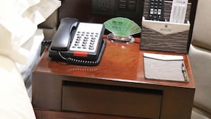 Une table de chevet en bois avec un téléphone, un ventilateur et un bloc-notes.