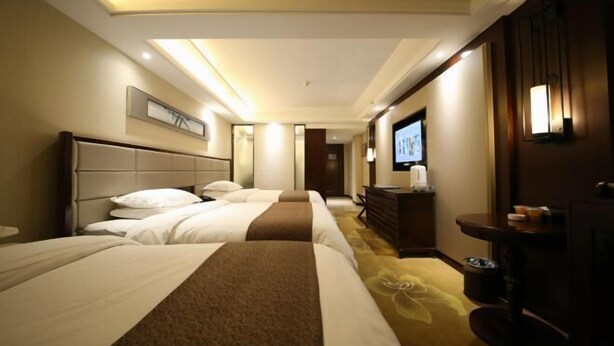 Une chambre d’hôtel avec trois lits, une télévision, un minibar et un sol recouvert de moquette.