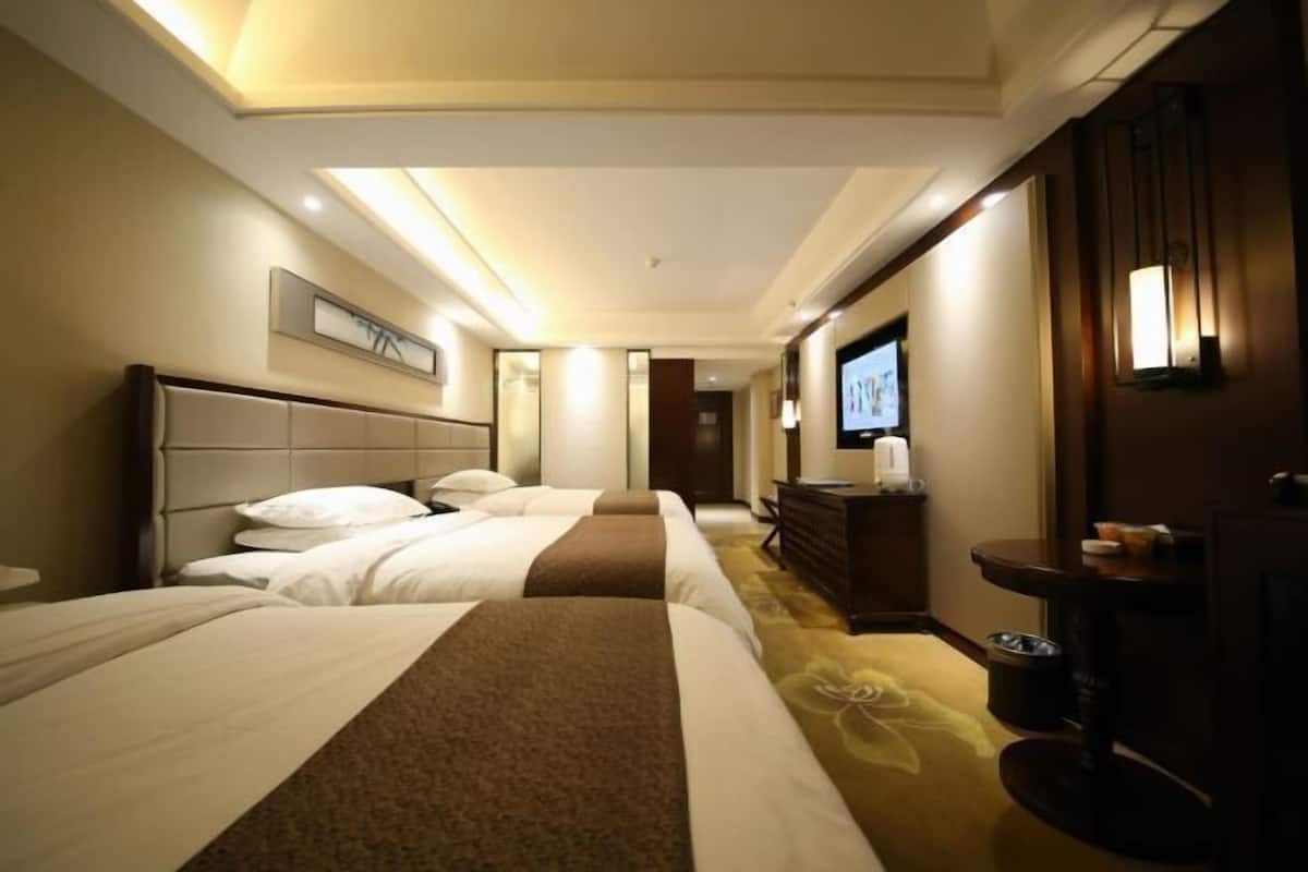 A hotel room with three beds, a TV, a minibar, and a carpeted floor.
