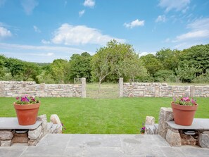 A stone wall with a grassy lawn and a tree in the background.