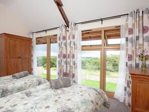 Une chambre avec deux lits, une armoire en bois, de grandes fenêtres et une vue sur la verdure.