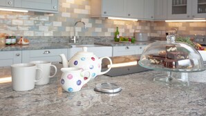 Een keuken met witte kasten, een betegelde achterwand, een koffiezetapparaat en een glazen taartplateau met brownies.