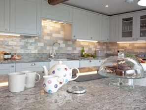 A kitchen with white cabinets, a tiled backsplash, a coffee maker, and a glass cake stand with brownies.