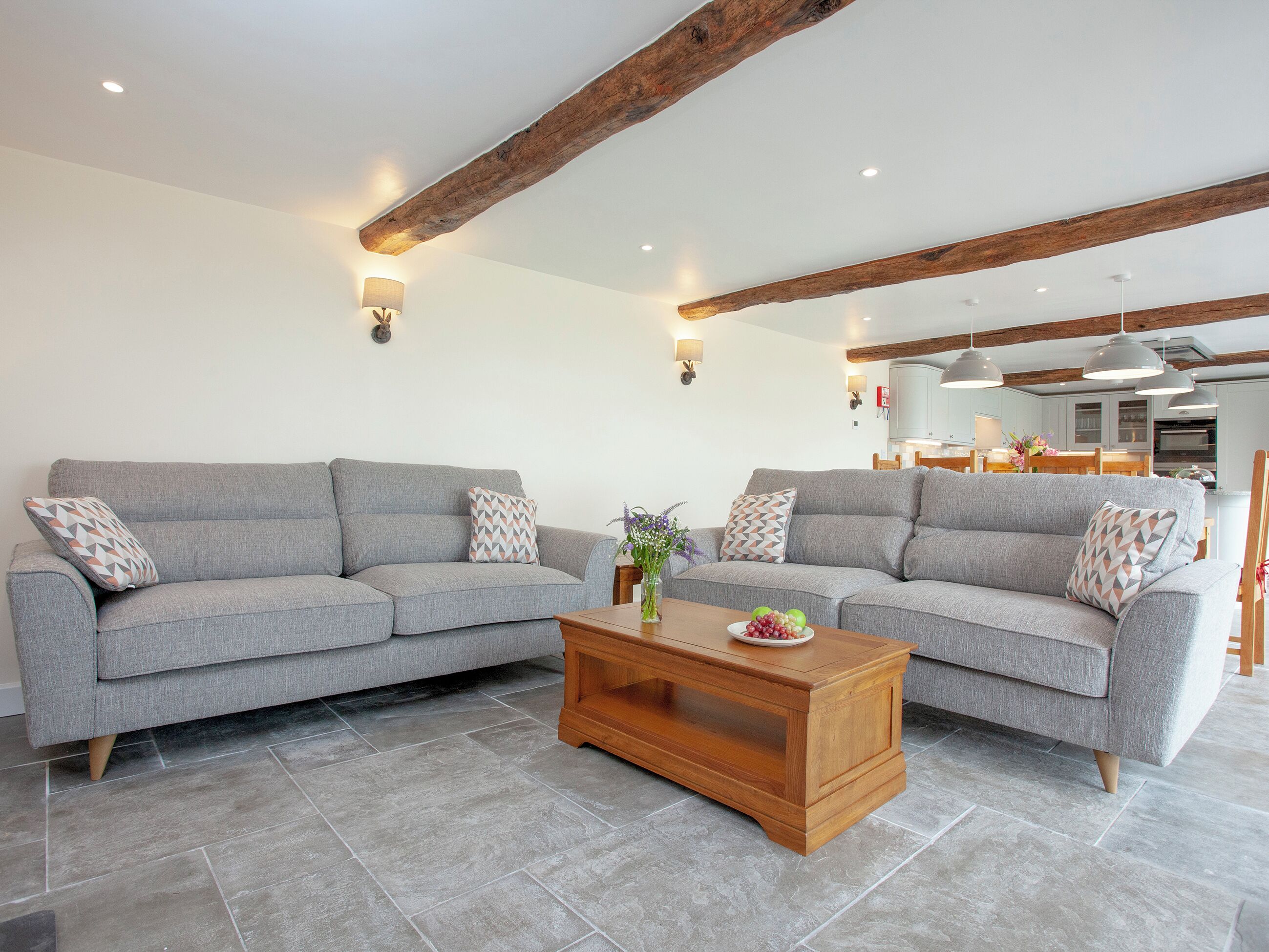A living room with two grey sofas, a wooden coffee table, and a kitchen in the background.
