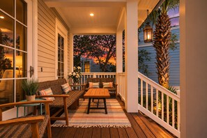 A covered porch with a wooden table and chairs, a wicker sofa, and a railing. - Stunning 30A Home-Pool, Bikes, Golf Cart, Pickleball, AC, 5 mins to the Beach (Santa Rosa Beach)