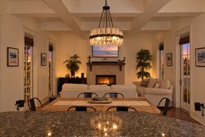 A spacious dining area with a large granite table, a fireplace, and a chandelier. - Stunning 30A Home-Pool, Bikes, Golf Cart, Pickleball, AC, 5 mins to the Beach (Santa Rosa Beach)