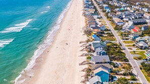 An aerial view of a coastal residential area with houses along the beach, a clear sky, and the ocean. - Keeping It Salty #101 Oceanfront Duplex, Private Beach Access, Dogs Allowed! (Surf City)