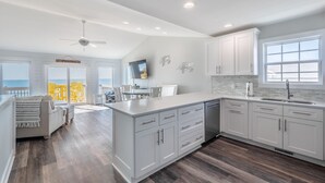 A modern kitchen with white cabinetry, a large island, and a view of the ocean. - Keeping It Salty #101 Oceanfront Duplex, Private Beach Access, Dogs Allowed! (Surf City)