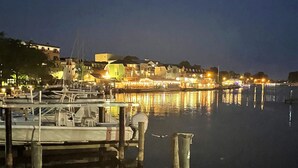 Uma marina à noite com barcos atracados, água calma e edifícios cujas luzes se refletem na água.