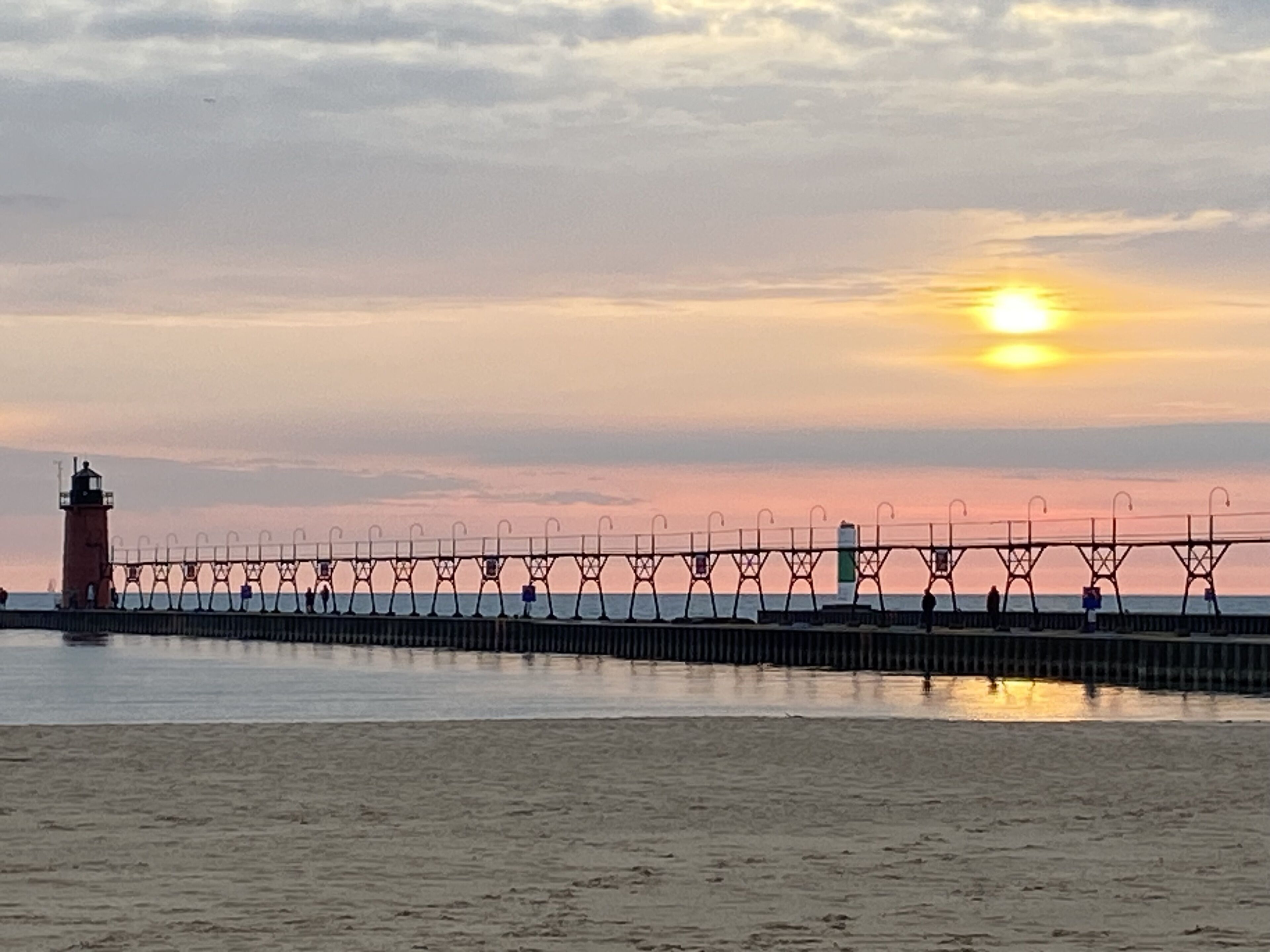 Tramonto sulla costa con un faro e un molo che si protende nell'acqua.
