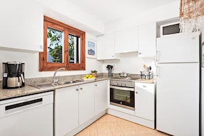 Eine moderne Küche mit weißen Schränken, einem eingebauten Backofen, einem Geschirrspüler und einem Fenster mit Blick auf Bäume.