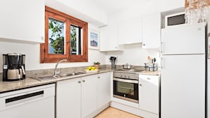 Une cuisine moderne avec des meubles blancs, un four encastré, un lave-vaisselle et une fenêtre donnant sur la verdure.
