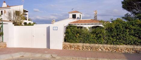 A villa with a white facade, a stone wall, and a tiled roof.