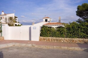 Una villa con fachada blanca, muro de piedra y tejado de tejas.
