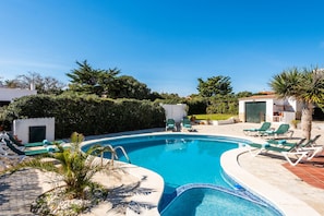 Ein Pool mit Liegestühlen, umgeben von Grünflächen und einem weißen Gebäude.