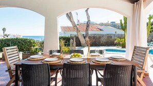 Un espace extérieur aménagé pour prendre les repas, avec vue sur la mer et une piscine.
