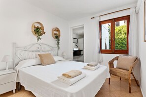 Un dormitorio ordenado con una cama grande, un sillón de mimbre y dos espejos fijados a la pared.