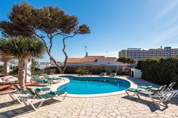 Una piscina con sillones de descanso, una palmera y un edificio con el letrero 'GLOBALES'.