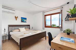Ein Schlafzimmer mit Bett, Nachttisch, Lampe und Meerblick durch ein Fenster.