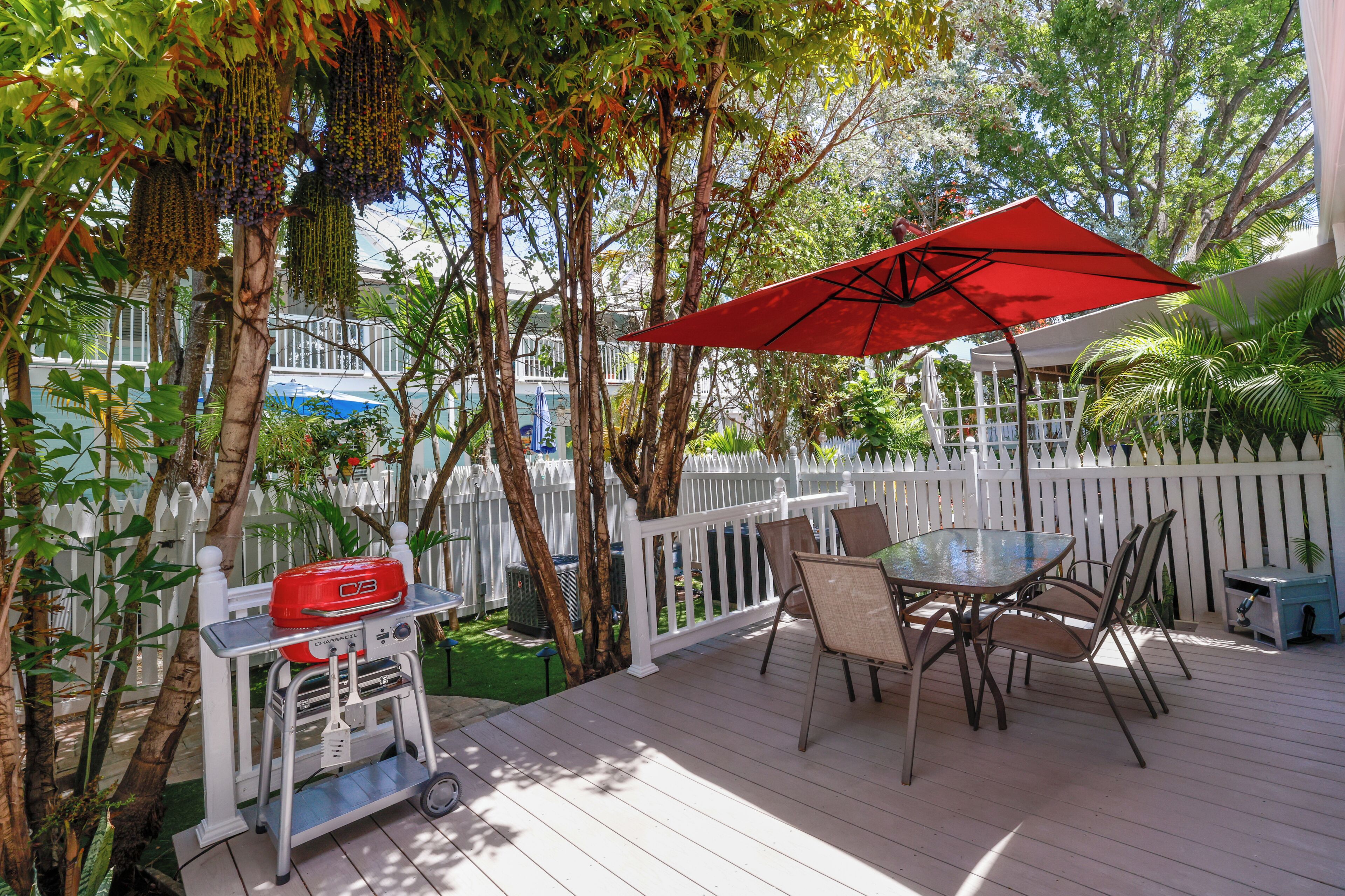 A covered outdoor patio with a table and chairs, a barbecue grill, and a white picket fence.