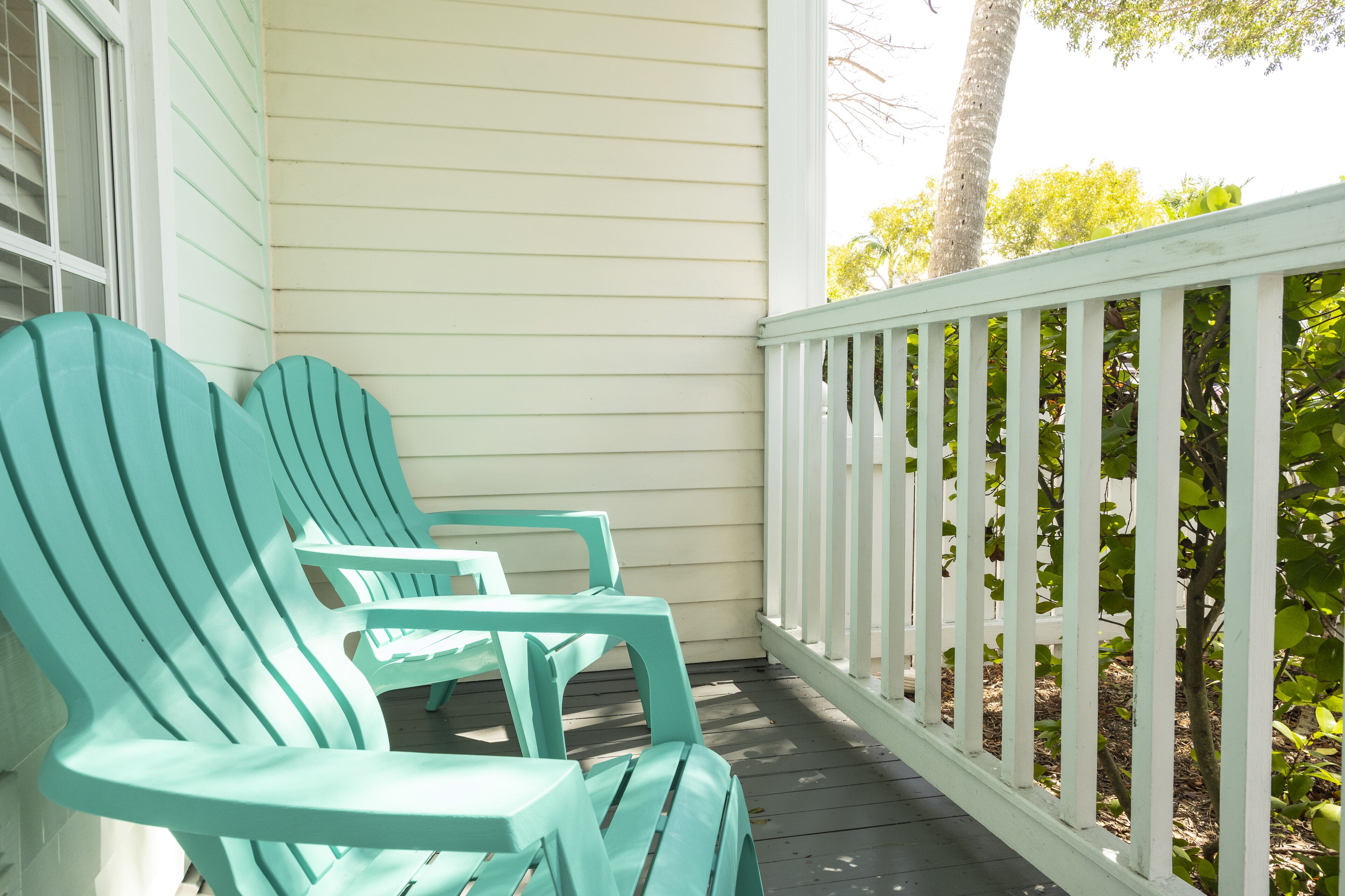 A porch with teal Adirondack chairs and a white railing.