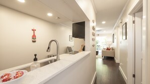 Eine moderne Küche mit weißer Arbeitsplatte, Spüle aus Edelstahl und einem schwarzen Wasserhahn. Auf der Arbeitsplatte steht eine Handseifenflasche.
