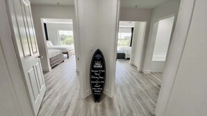 Un couloir avec un panneau représentant une planche de surf, un plancher en bois et un lit en arrière-plan.