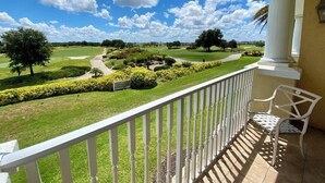 Un balcon donnant sur un terrain de golf, une chaise blanche et une balustrade blanche.