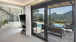 Un salón moderno con un televisor de pantalla plana, un ventanal de vidrio que da a un balcón con piscina y mobiliario exterior.