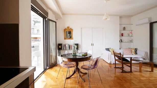 Una sala moderna con comedor, un sofá y una mesita de centro. Una ventana grande ofrece luz natural y vistas al exterior.