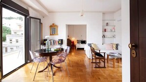 Un salon moderne avec un plancher en bois, un coin repas doté d’une table et de chaises en verre, un canapé et une bibliothèque.