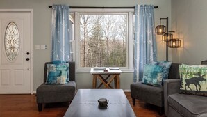 Un salon chaleureux avec une grande fenêtre, deux fauteuils, une table basse et une applique murale décorative.
