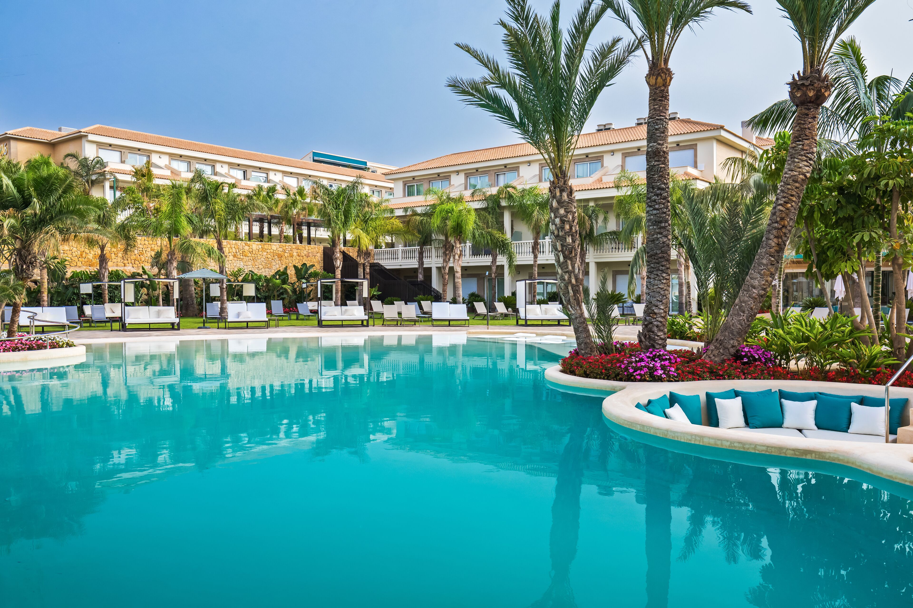 A resort pool area with a clear blue pool, palm trees, and lounge chairs.