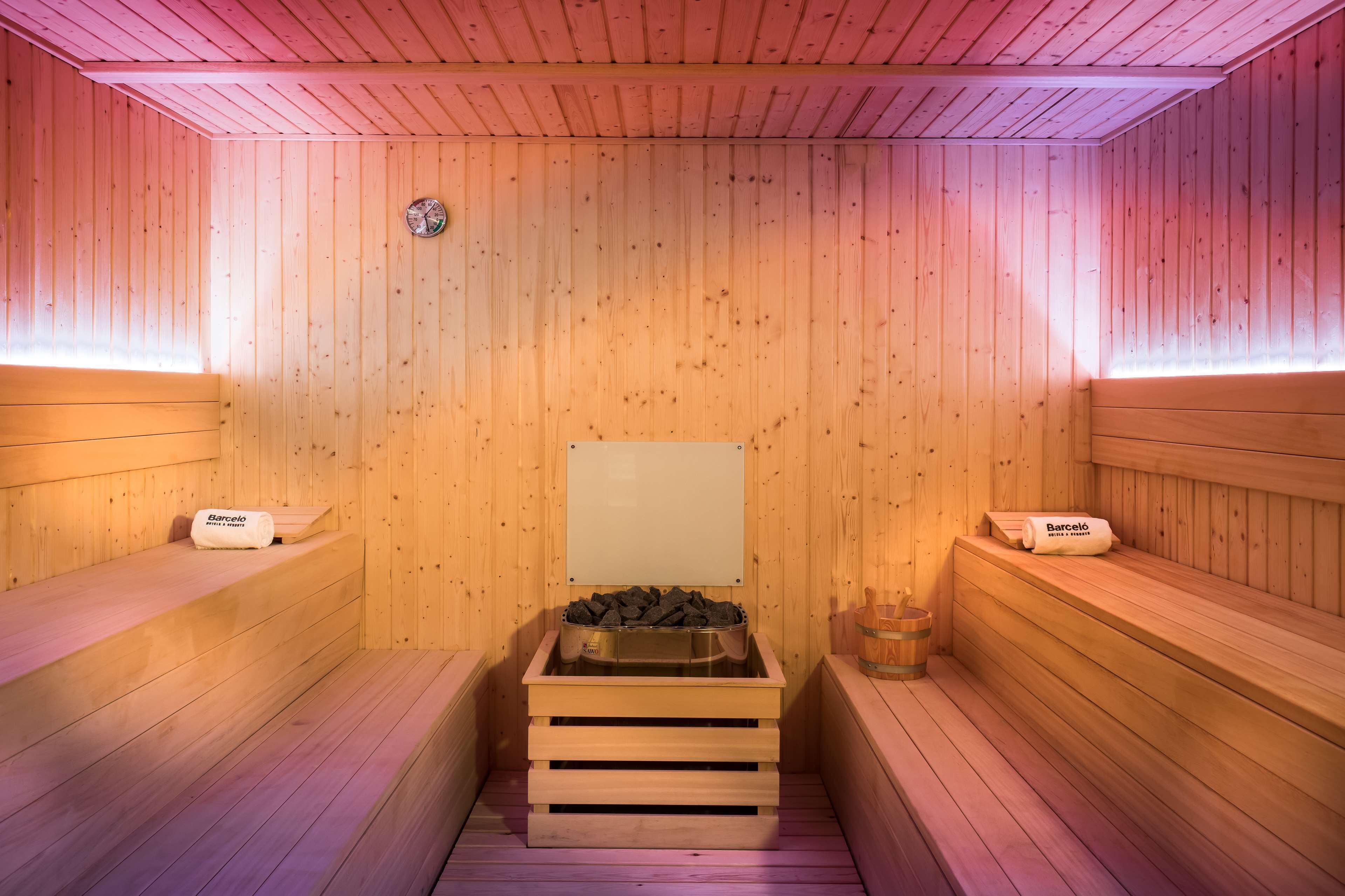 Una sauna de madera con bancos a ambos lados, un banco central con una chimenea y un reloj en la pared.