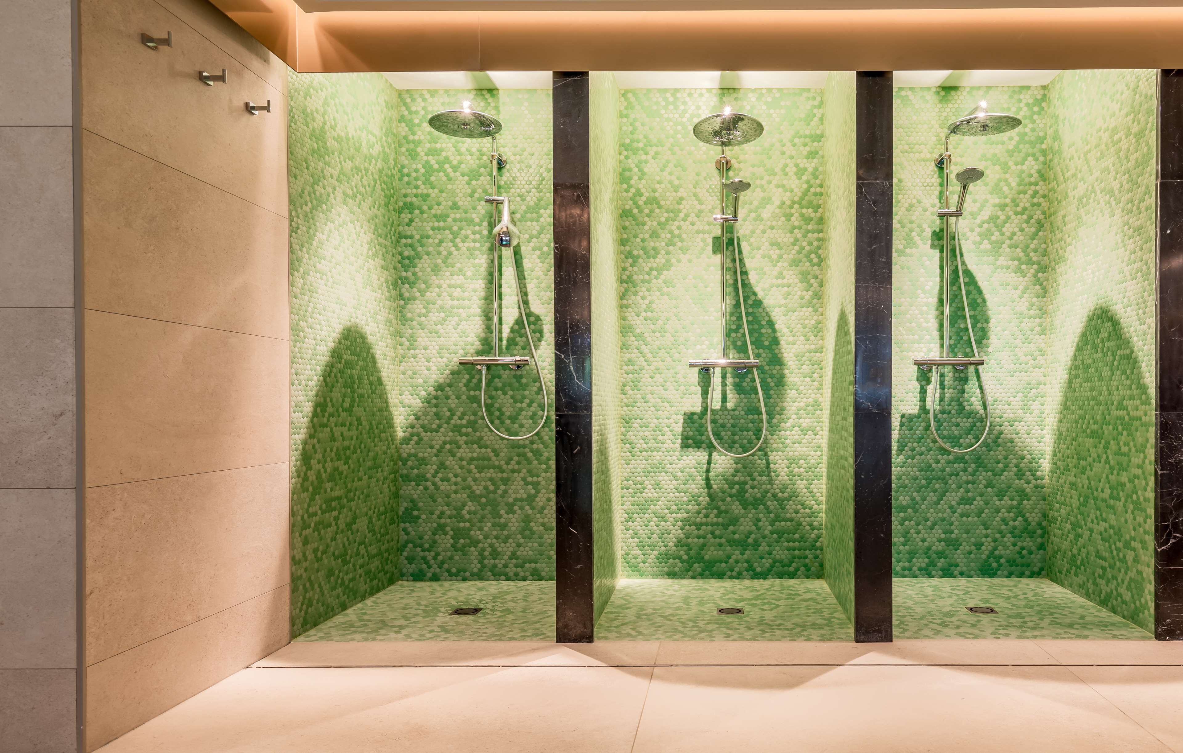 Ein modernes Badezimmer mit einer Wand in Grüntönen und einer Struktur, einem großen Spiegel und einem Duschbereich mit Handbrause.