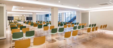 A spacious conference room with rows of chairs, large windows, and a staircase in the background.