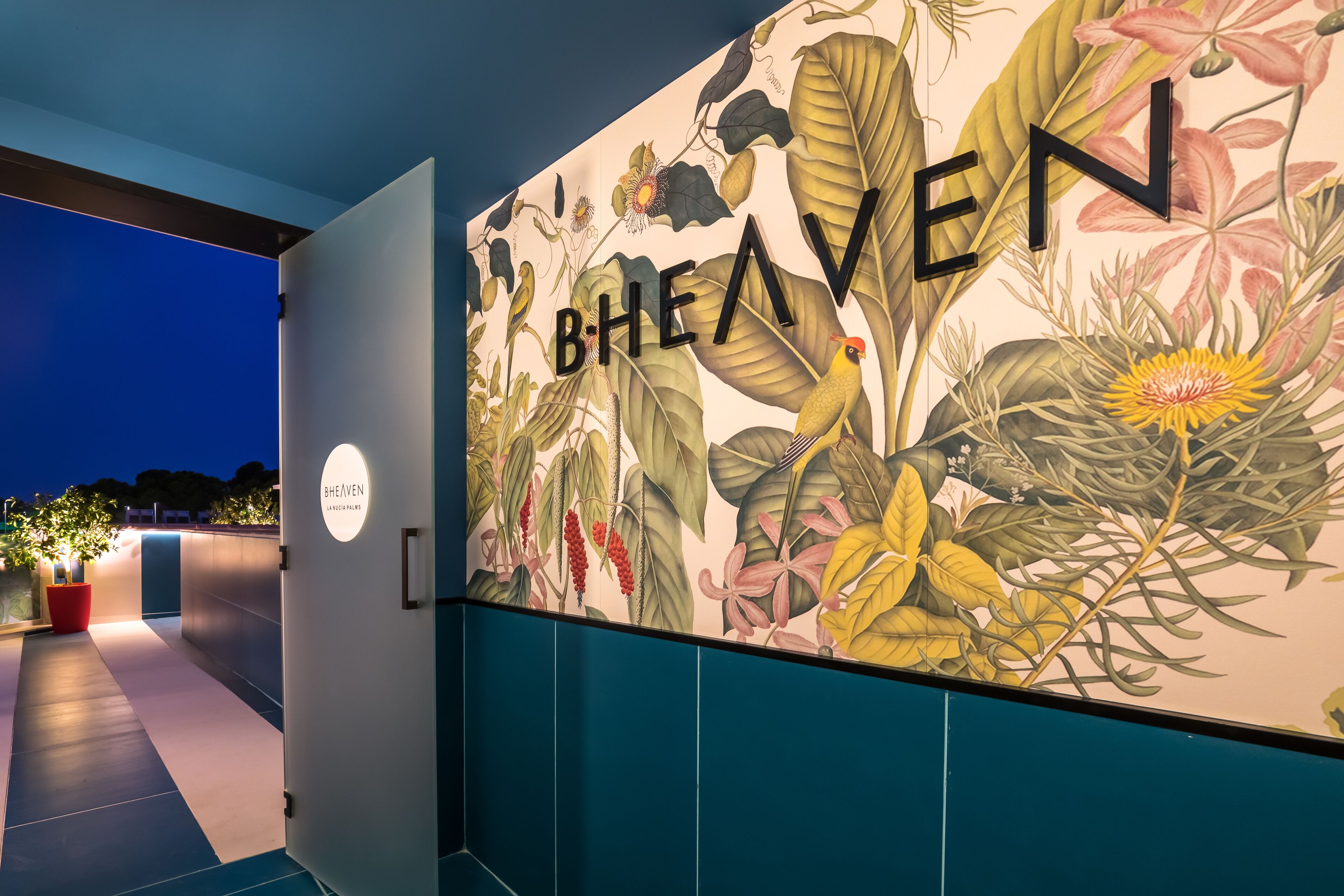 A hallway with a mural of tropical plants and the word "BHEAVEN" prominently displayed.
