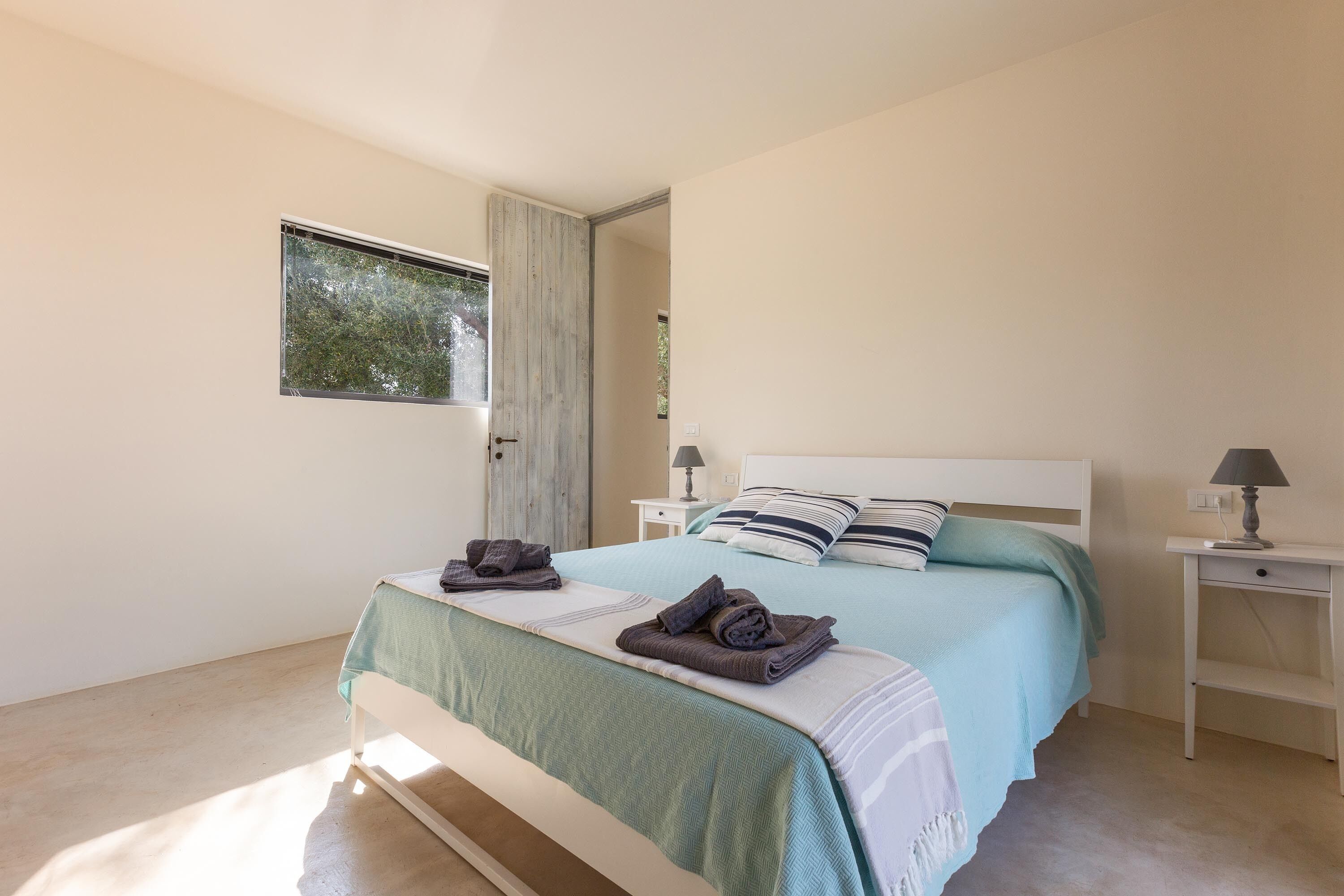 A bedroom with a bed, two bedside tables, a window, and a door.