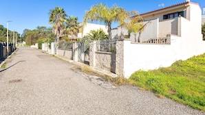 Un carrer residencial amb una casa blanca, un mur de pedra i palmeres.