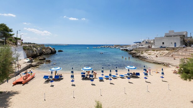 Una platja amb aigua turquesa cristal·lina, un vaixell i diverses paraigudes i gandules.