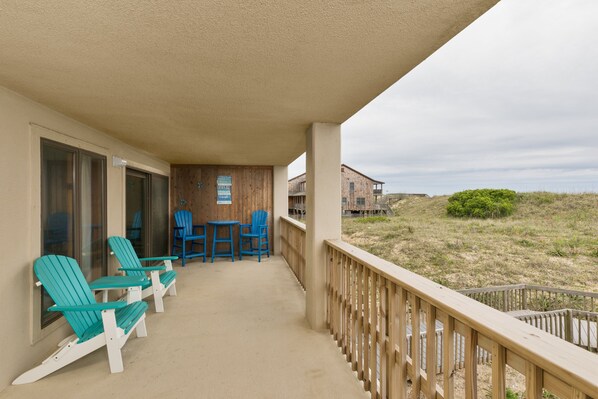 Un balcón con sillas Adirondack azules y una mesa, con vista a una playa con dunas.