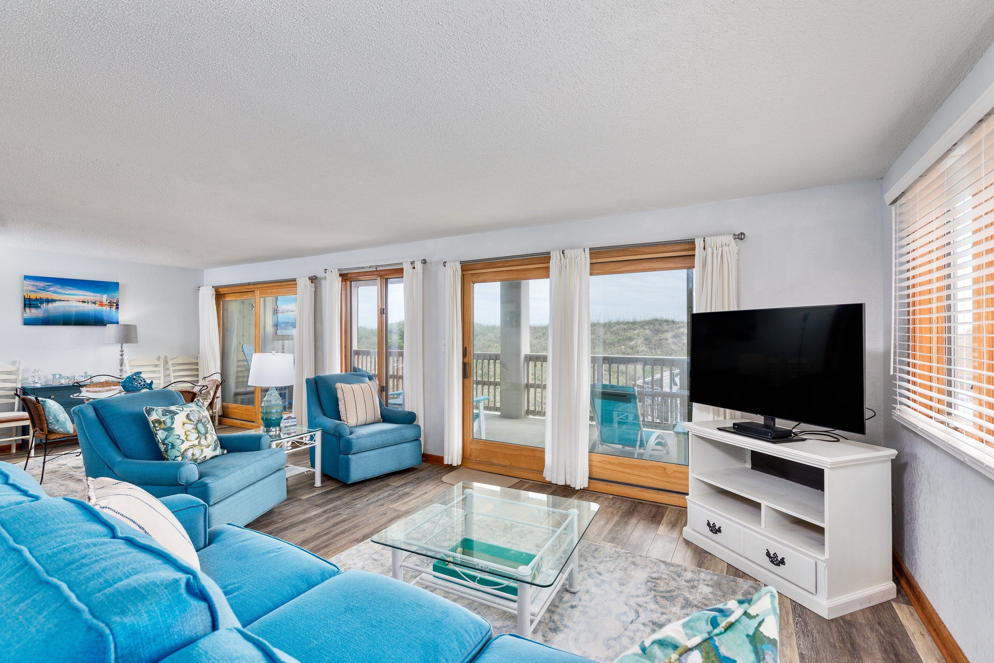 A spacious living room with a large TV, blue sofas, and a glass coffee table.