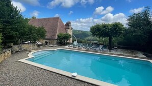 A swimming pool with lounge chairs, a stone building, and a mountainous backdrop.