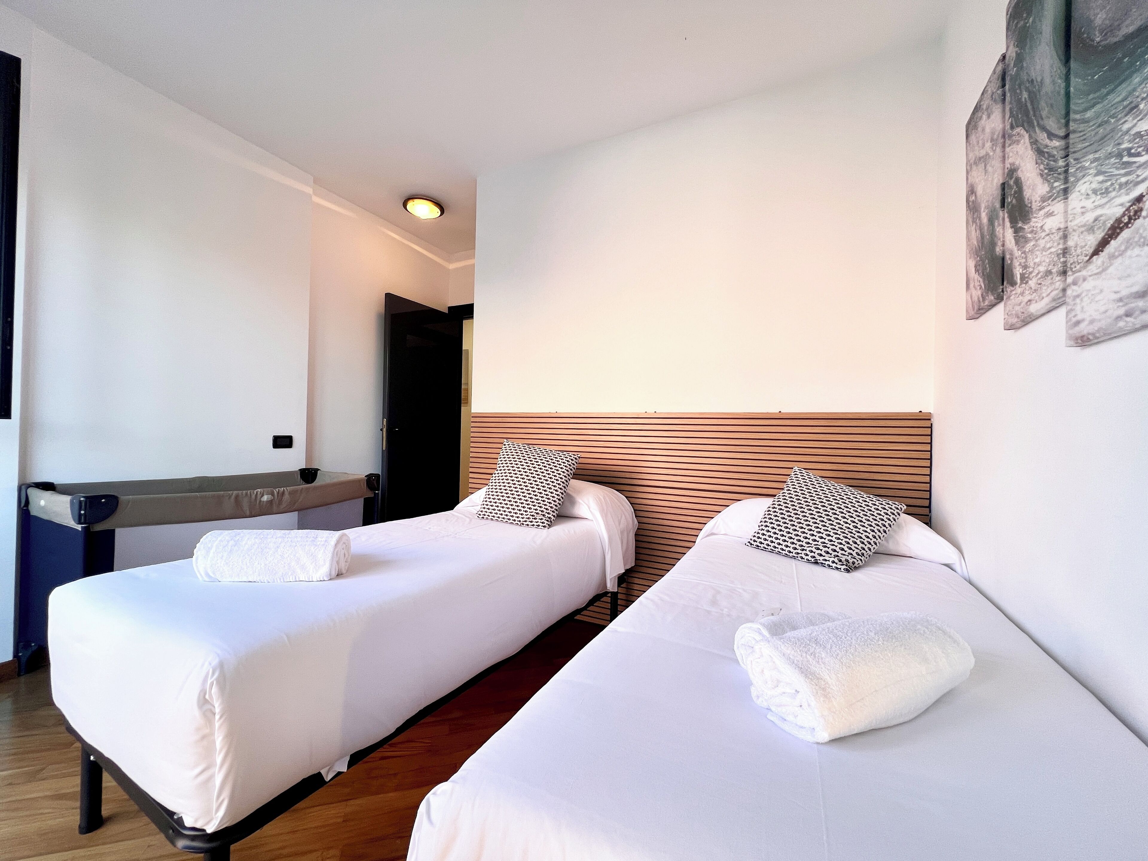 A hotel room with two single beds, a wooden headboard, a small bedside table, and a wall-mounted artwork.